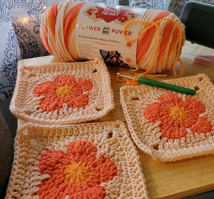 Colorful crocheted flower squares with yarn and a crochet hook on a wooden table.