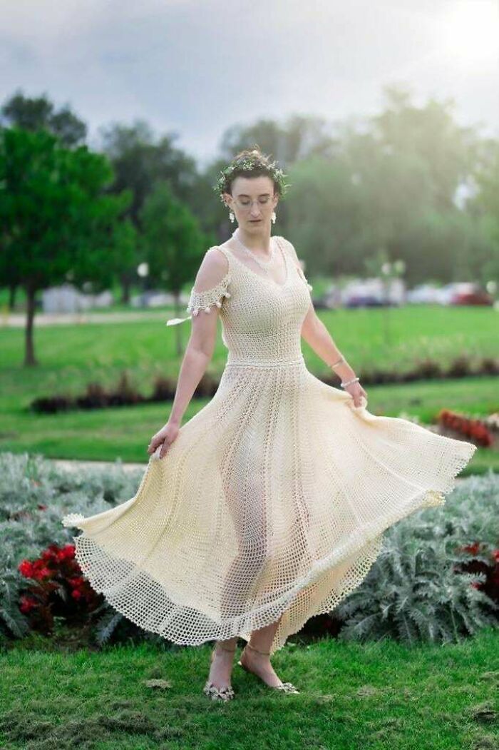 Woman in a crocheted dress, gracefully spinning in a lush green park setting.