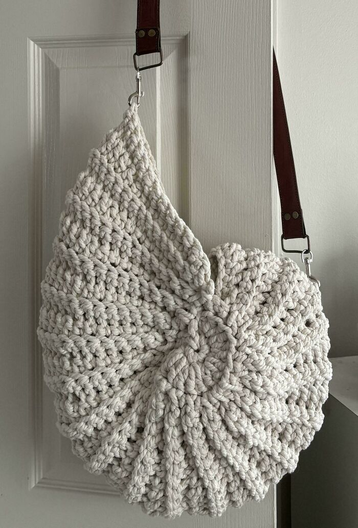 Crocheted seashell-shaped bag with a brown strap hanging on a door.