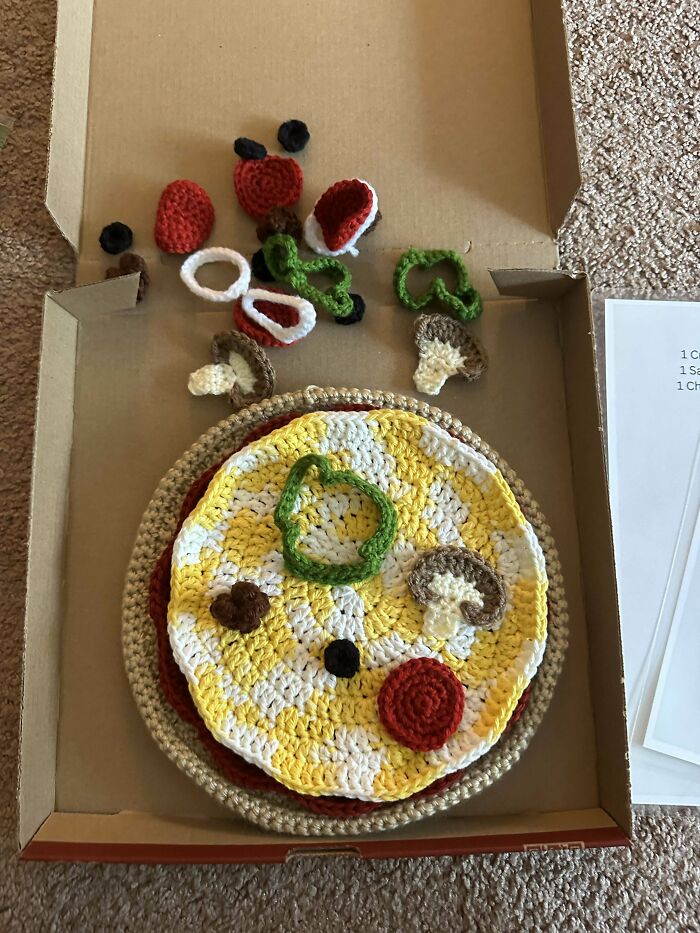 Crocheted pizza with yarn toppings in an open box, showcasing creative crochet art.