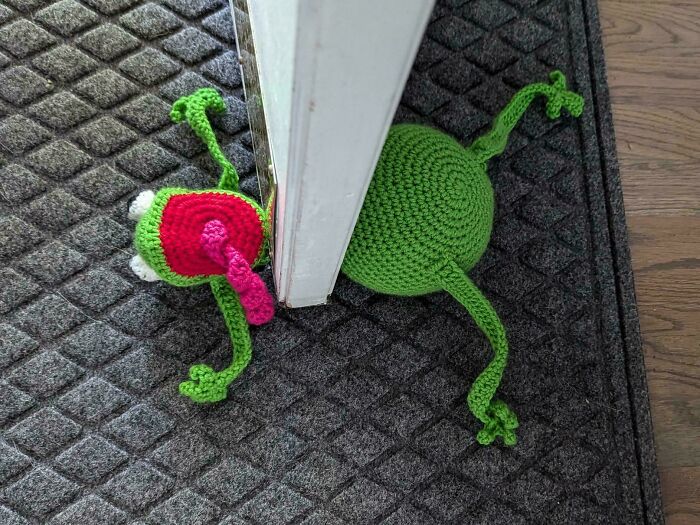 Crocheted frog doorstop with bright colors, creatively placed under a door.