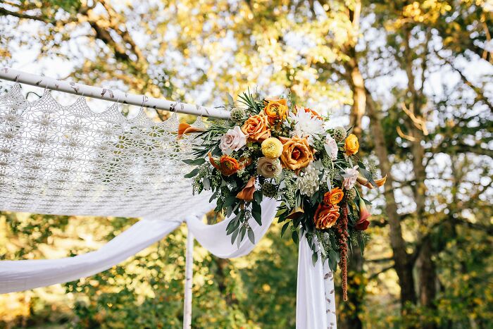 Crocheted canopy with floral arrangement in an outdoor setting, featuring intricate patterns and vibrant flowers.