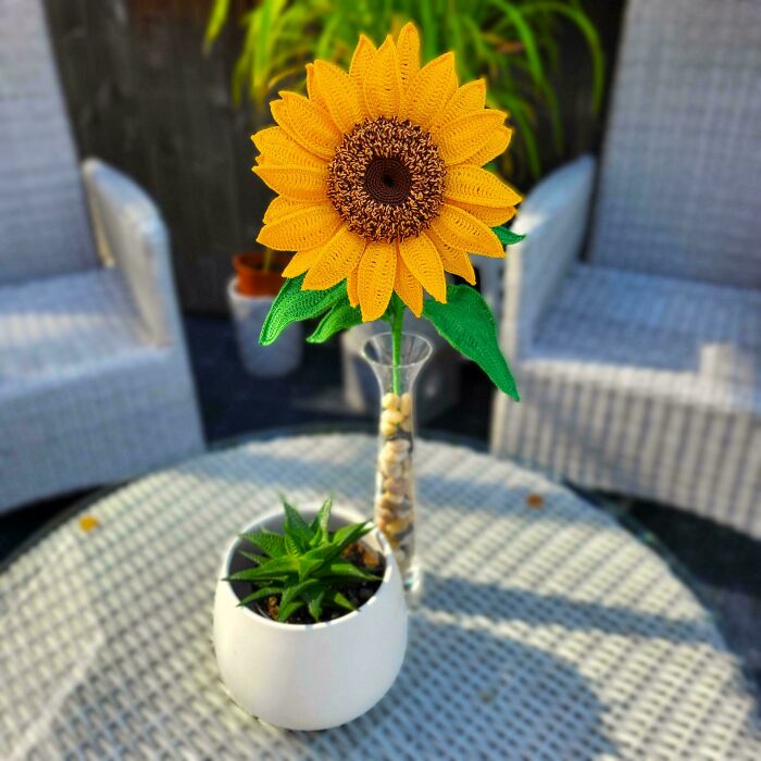 Crocheted sunflower in a vase on a patio table with a small potted plant.