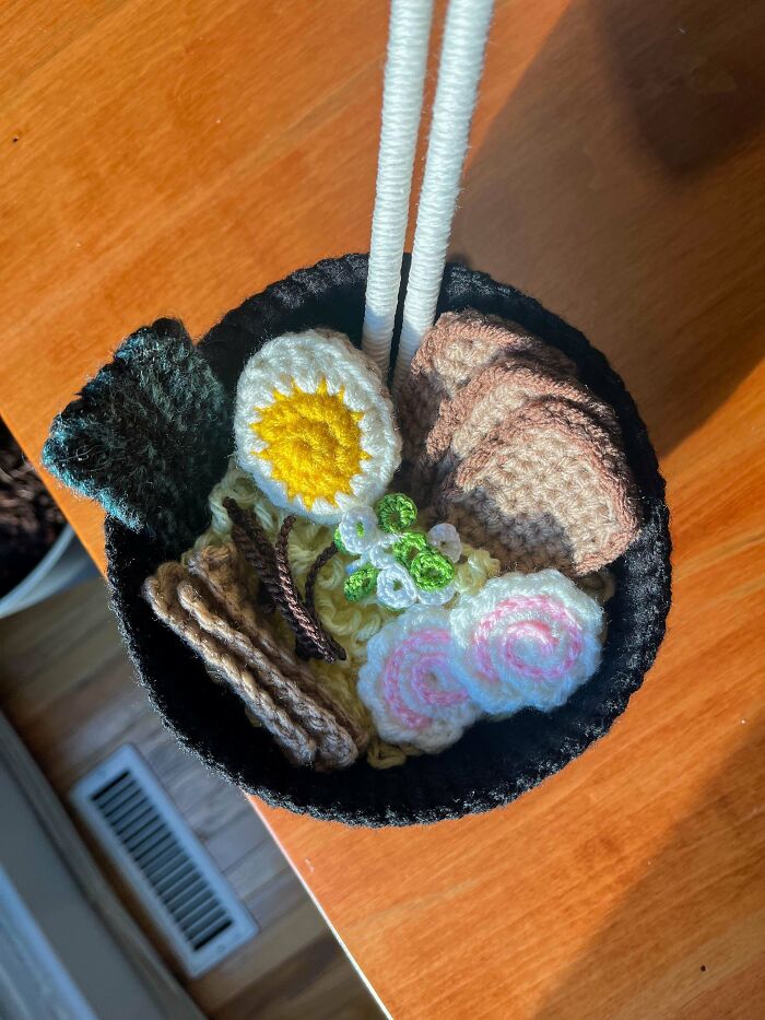 Crocheted bowl of ramen with intricate details on a wooden table.