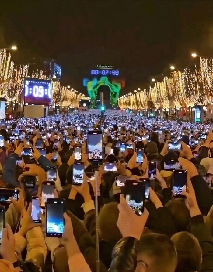 A crowd of people capturing an event on smartphones under festive lights, illustrating humans-of-capitalism-pictures.