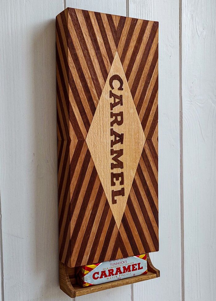 Wooden caramel dispenser on a wall, showcasing British humor with a Tunnock's caramel wafer visible at the bottom.