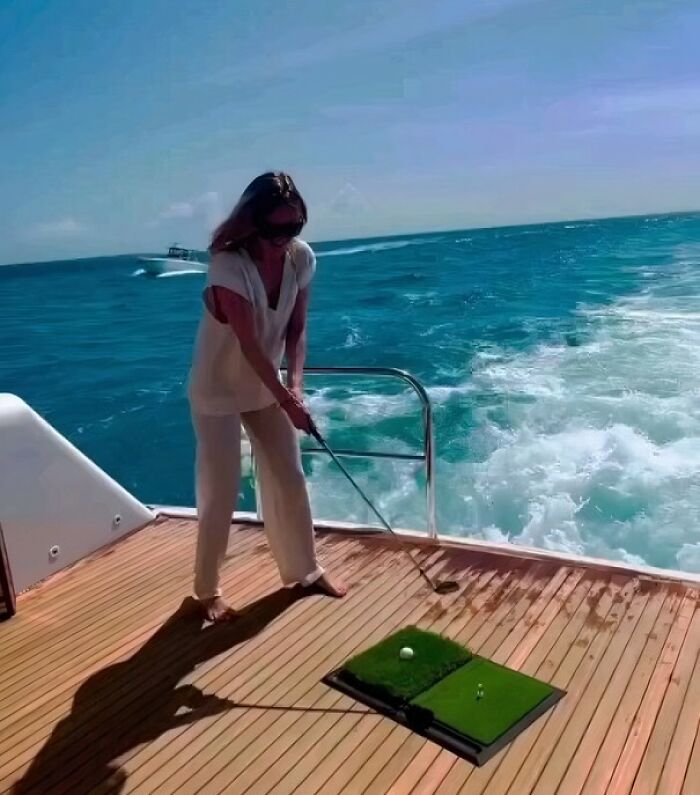 Person golfing on yacht deck at sea, embodying leisure in humans-of-capitalism-pictures.