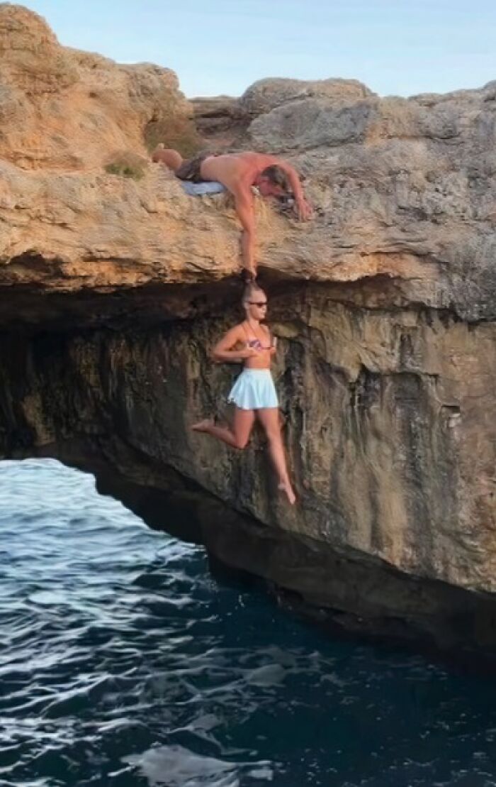 Two people engaging in a daring rock-climbing stunt above water, illustrating aspects of humans of capitalism pictures.