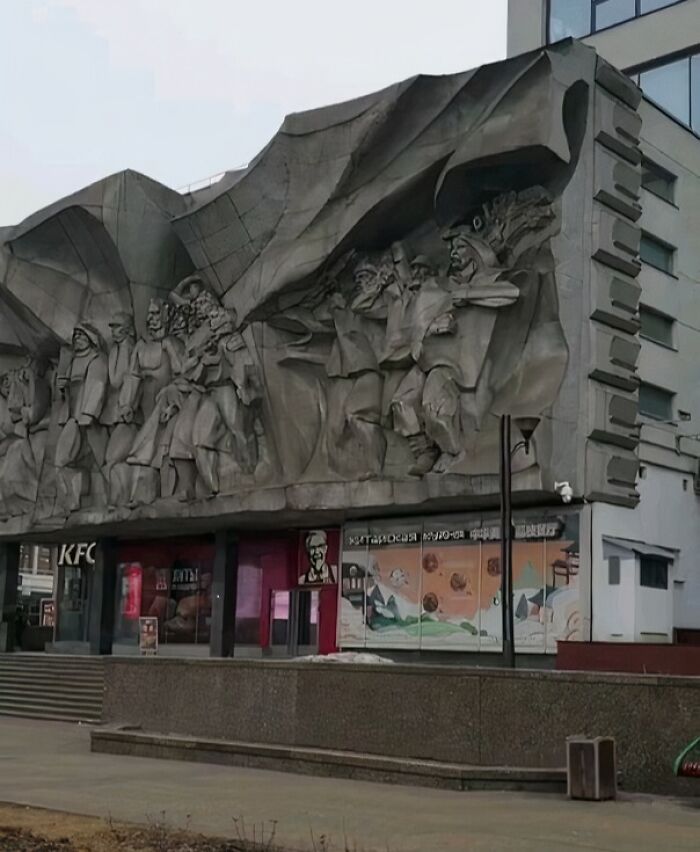 Concrete mural above a KFC store representing humans in capitalism-themed artistic expression.