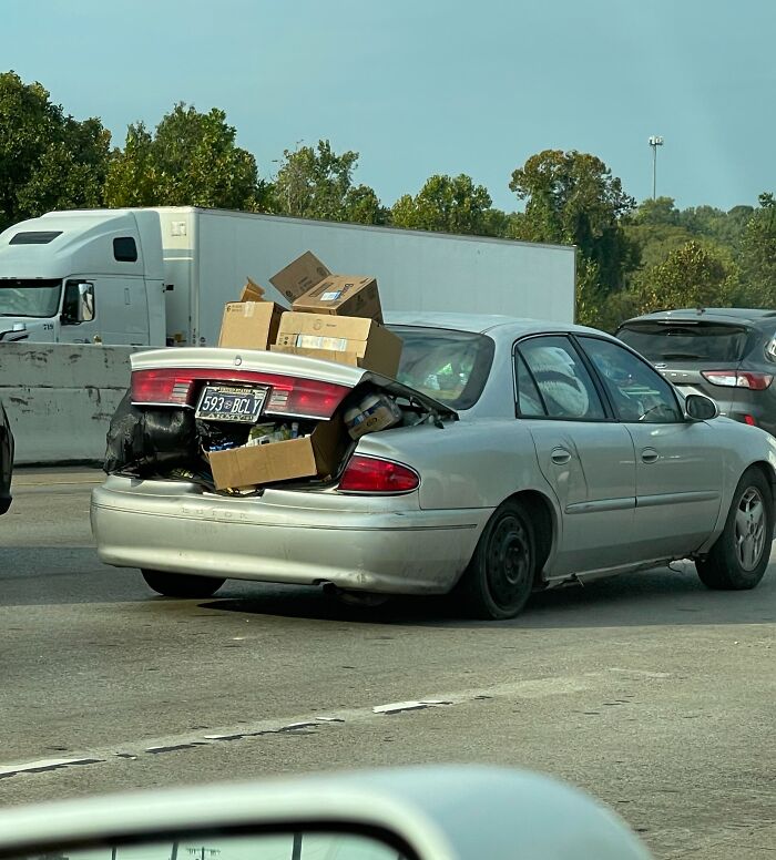 Car on highway with trunk overloaded with boxes, exemplifying poor driving behavior.