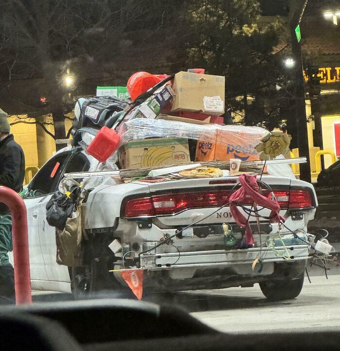 Overloaded car with comical assortment of items strapped on, highlighting a typical "Idiots-In-Cars" scenario.