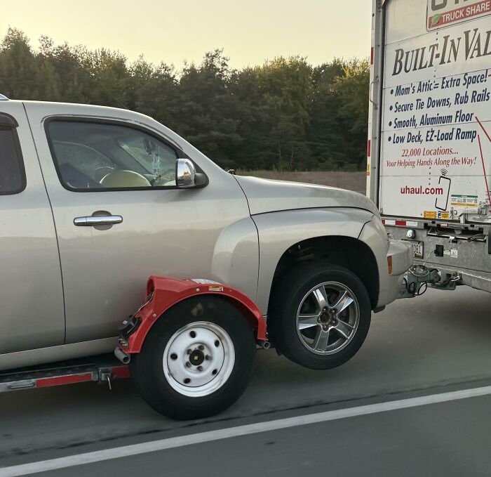 Car improperly loaded onto a U-Haul trailer, showing one wheel off the hitch, illustrating unsafe driving practices.