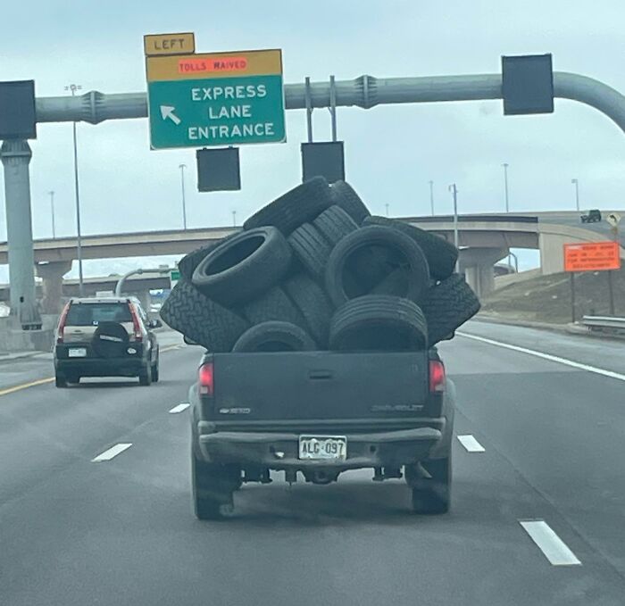 Pickup truck overloaded with tires on highway, illustrating risky driving behavior related to "idiots-in-cars."