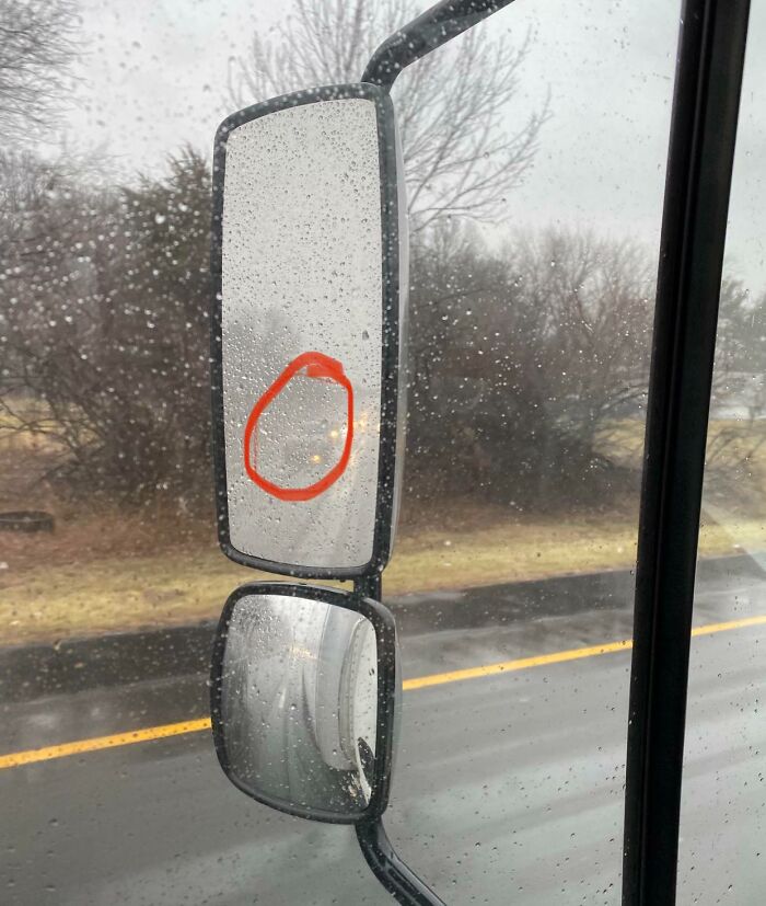 Truck side mirror with red circle highlighting a car, illustrating poor visibility on a rainy road.