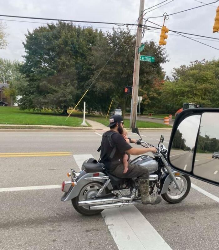 Person riding motorcycle with a small child sitting in front, stopped at a traffic light on Eastman Ave.