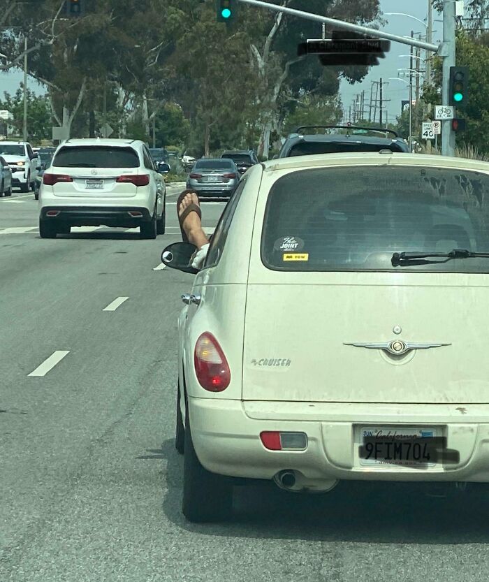 Foot sticking out of a white car window while driving on a busy street, representing classic idiots in cars behavior.