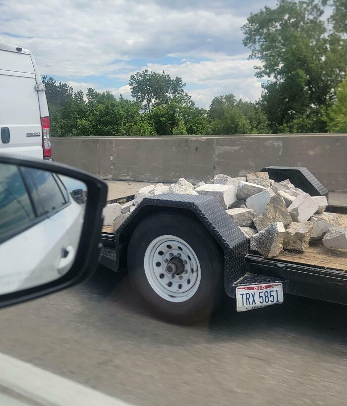 Trailer loaded with loose rocks on the road, illustrating careless driving behavior.