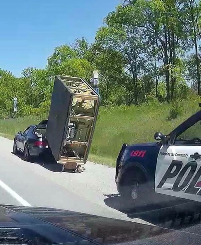 Car with precariously balanced furniture on the road, police vehicle nearby. Idiots in Cars moment captured on a highway.