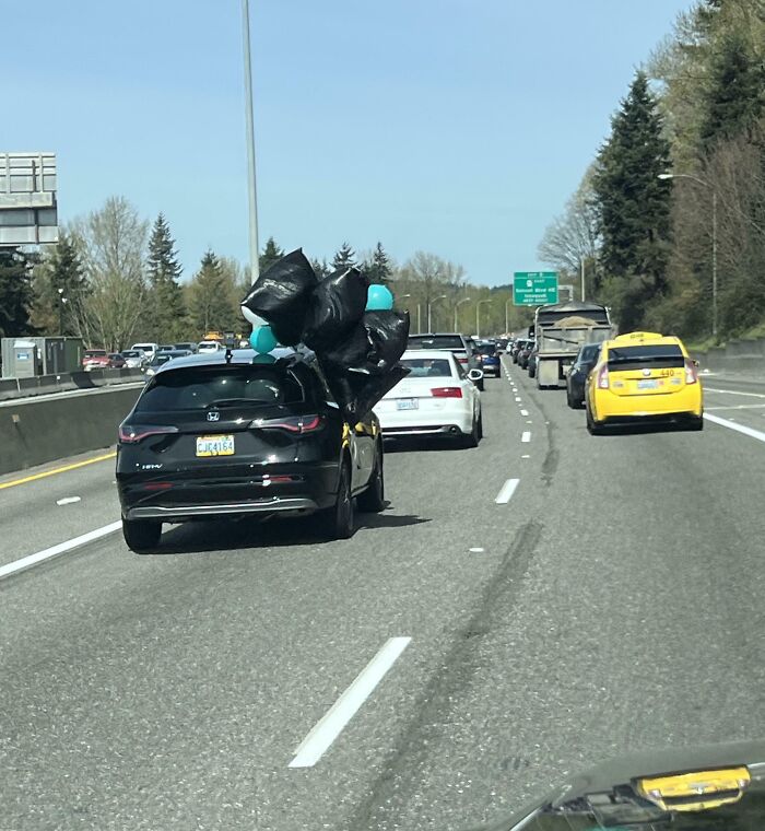 Car driving on highway with garbage bags tied to the roof, an unusual sight emphasizing poor decision-making.