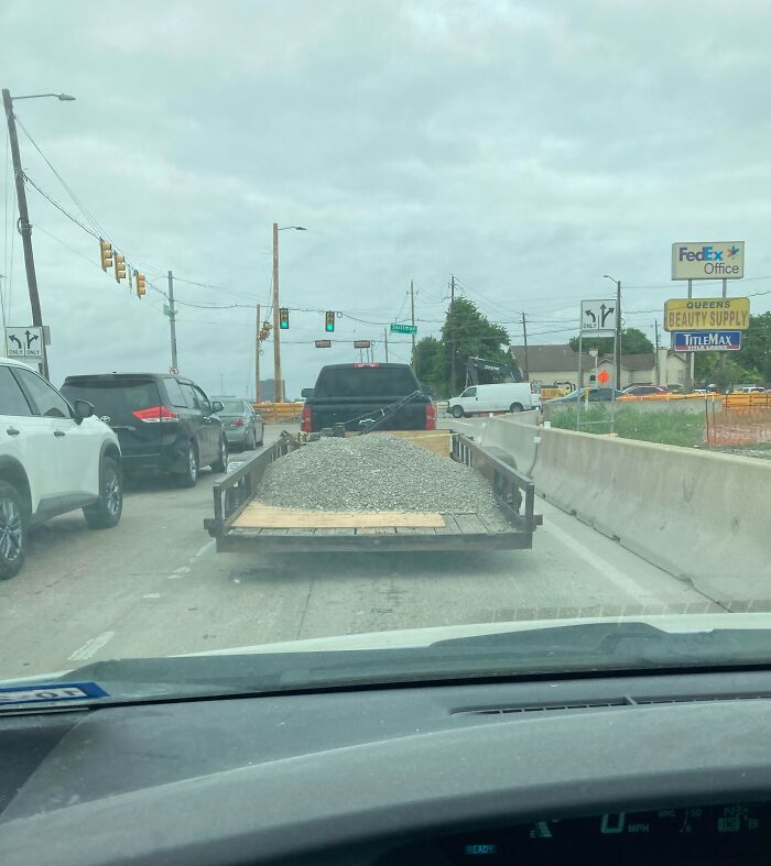 Truck hauling gravel precariously on a busy road, illustrating risky driving behavior from idiots in cars.