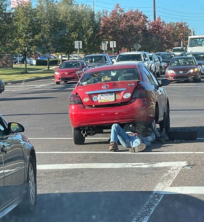 Person working under a car in the middle of a busy intersection, showcasing dangerous behavior typical of idiots in cars.