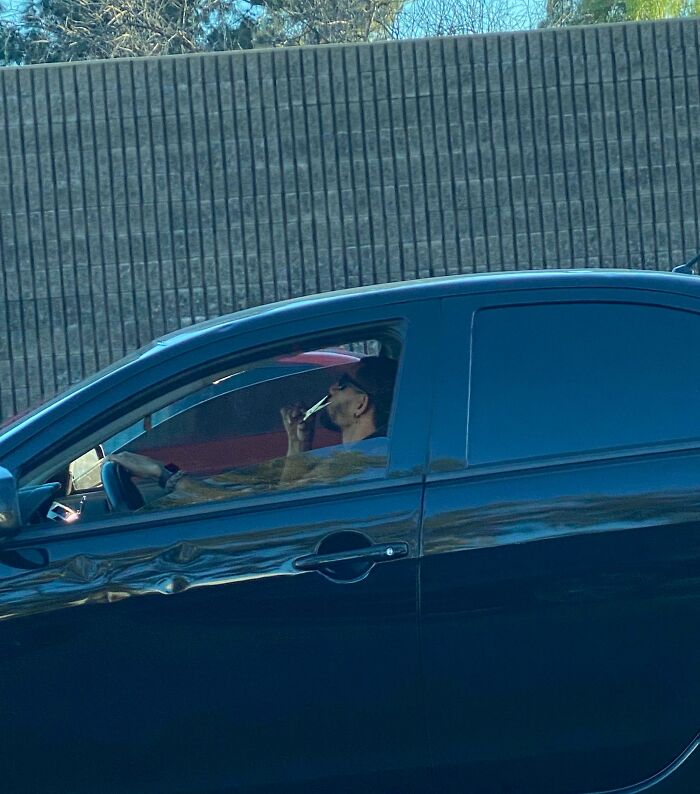 A person driving a car while distracted and using an electric toothbrush.