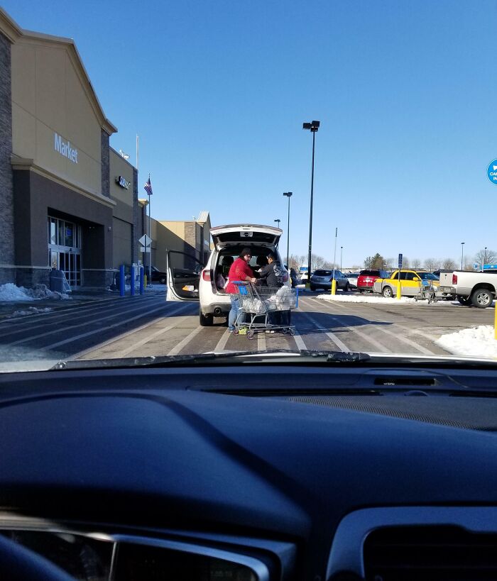 Car parked awkwardly in front of store entrance with open trunk and shopping cart blocking traffic, illustrating "Idiots in Cars."