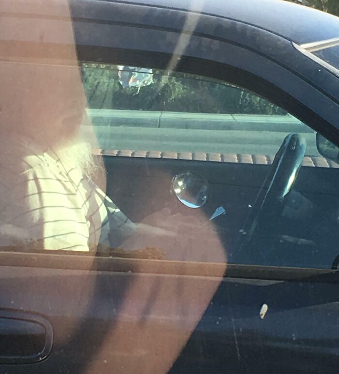 Person in car distracted by phone, reflecting "Idiots-In-Cars" concept.