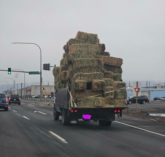 Overloaded truck with hay bales on the road, a classic Idiots-In-Cars scenario.