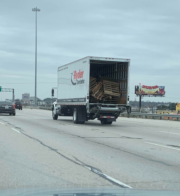 Open back of truck on highway, loaded with unsecured pallets, illustrating risky driving behavior related to "Idiots-In-Cars."