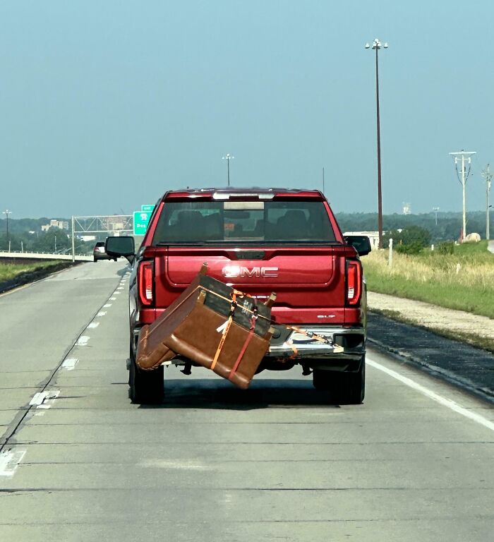 Red GMC truck driving with a couch precariously tied to the tailgate, illustrating poor transport decisions.