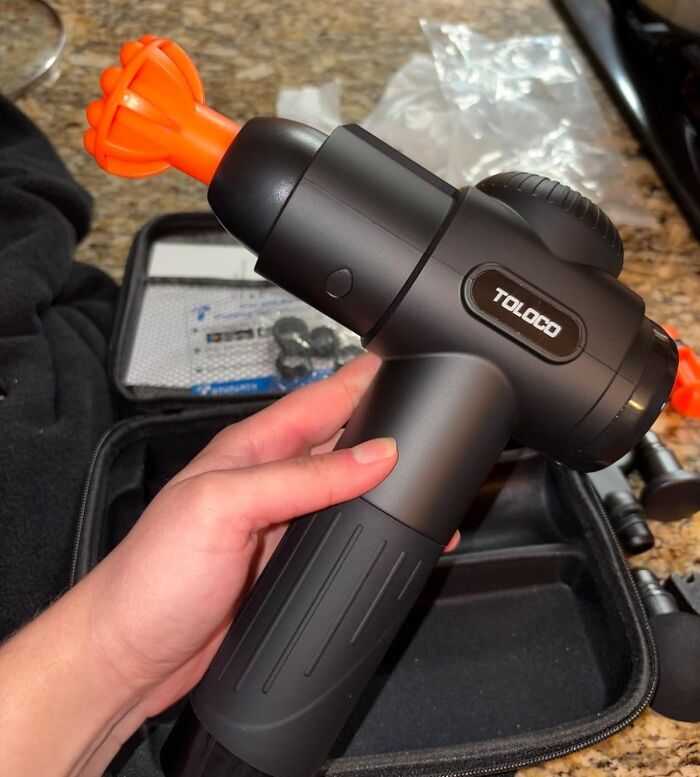 Massage gun held above a case on a countertop, showcasing winter discounts on Amazon deals.