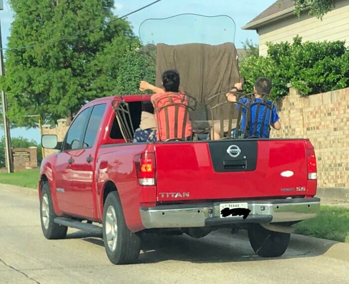 A red truck carrying people sitting on unsecured chairs in the truck bed, illustrating potential safety concerns for ignorant-parents.