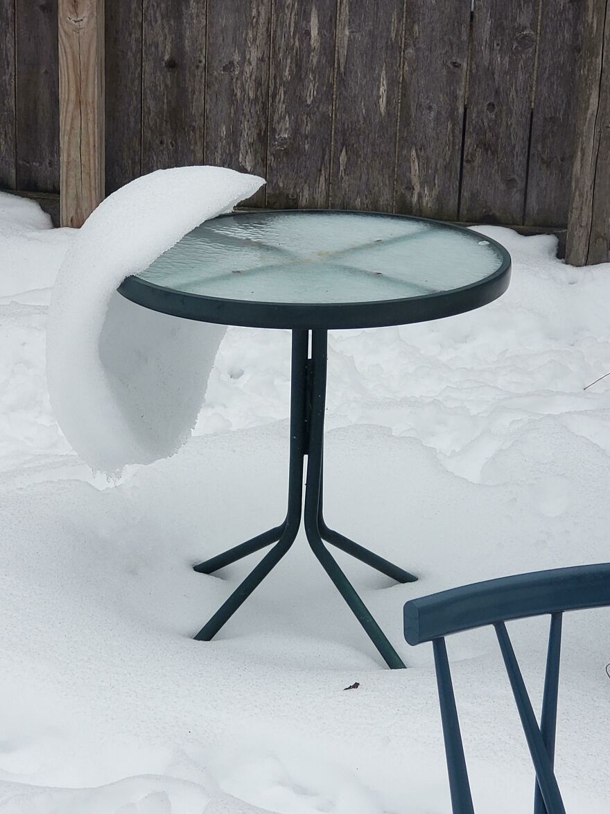 Snow curled on outdoor table, resembling accidental art.