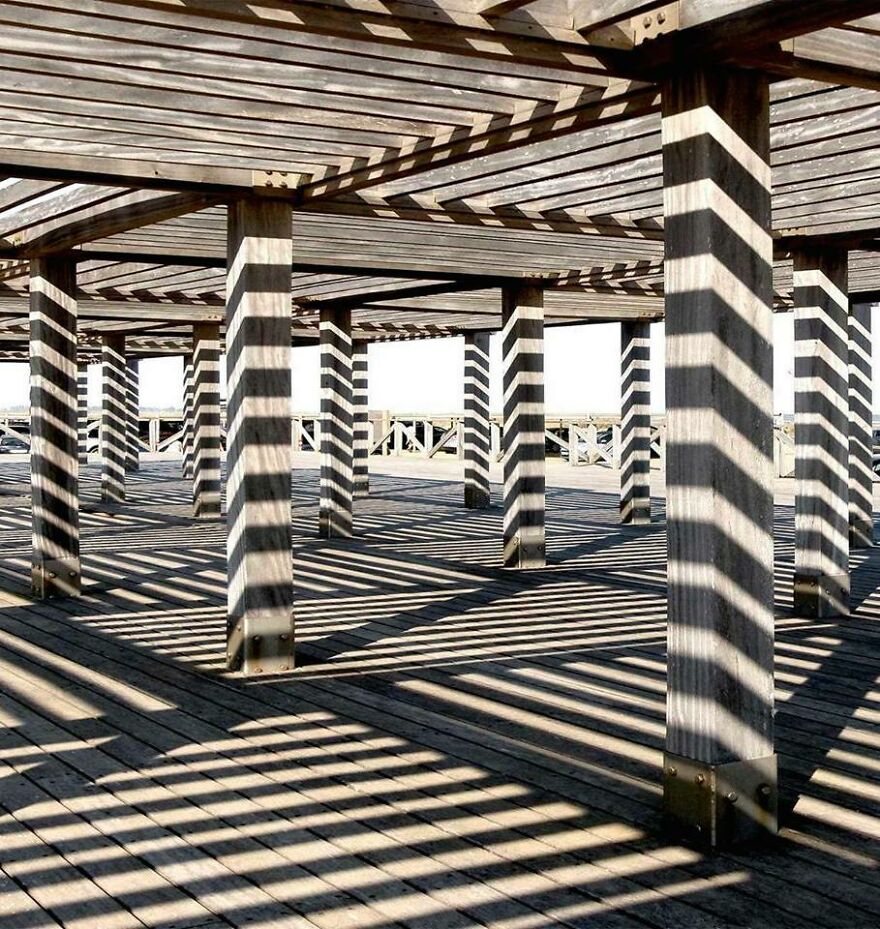 Geometric shadows cast by wooden beams create an accidental art effect on a sunlit deck.