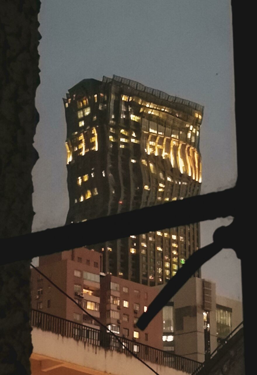 A distorted skyscraper lit up at night, seen through a window frame, showcasing accidental art.