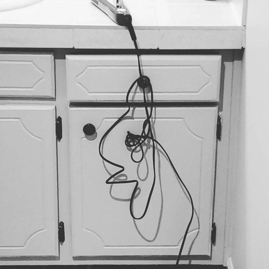 Accidental-Art-Pics: Hair straightener cord forms a face-like shape against a cabinet in black and white.