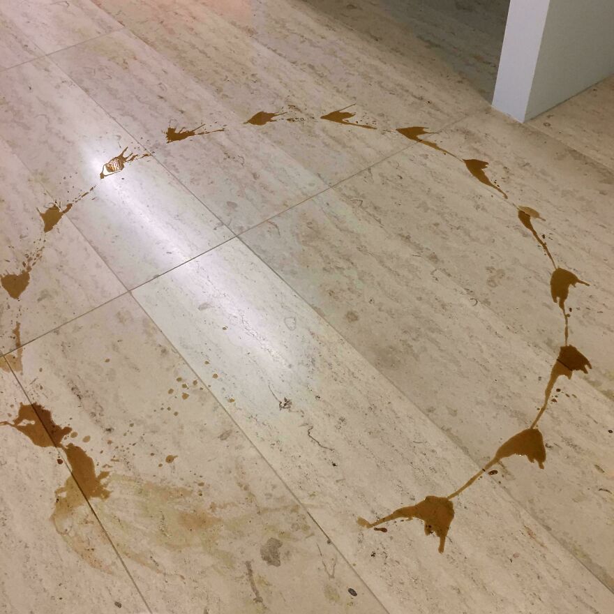 Circular coffee spill on marble floor creating accidental art pattern.