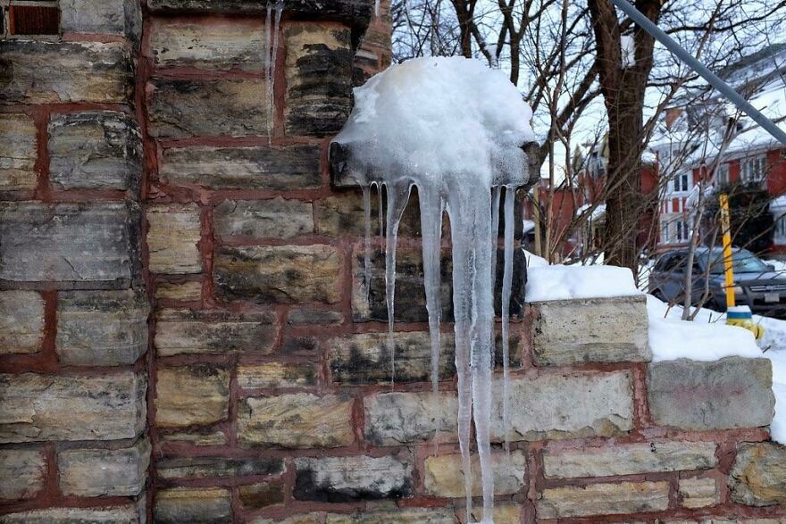 Icicles forming on a brick wall, creating a sculpture-like appearance.