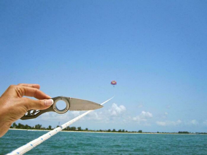 A hand playfully holds a knife, humorously pretending to cut a parasailing rope in this funny camera roll find.