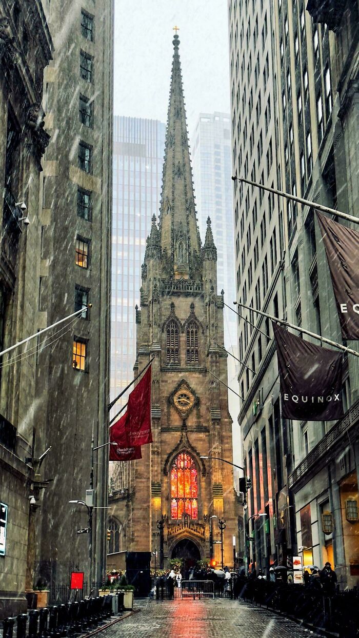 Gothic church facade in cityscape with snow falling, framed by tall buildings, highlighting fascinating architecture.