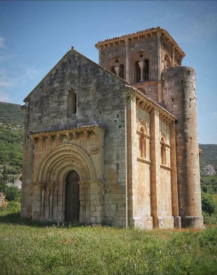 Ancient stone church surrounded by greenery under a clear sky, showcasing architectural details.