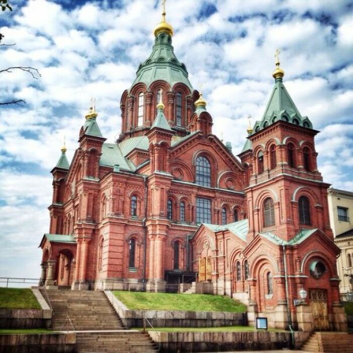 Red brick church with green domes against a cloudy sky, showcasing fascinating church architecture.