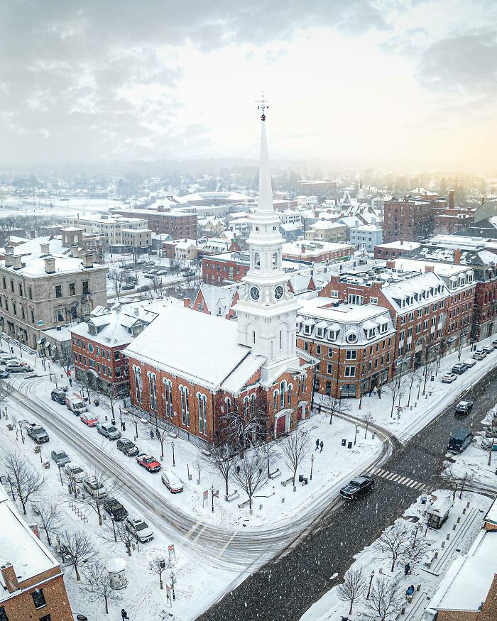 Snow-covered church in a winter cityscape, featuring a tall white steeple, capturing fascinating church photos.