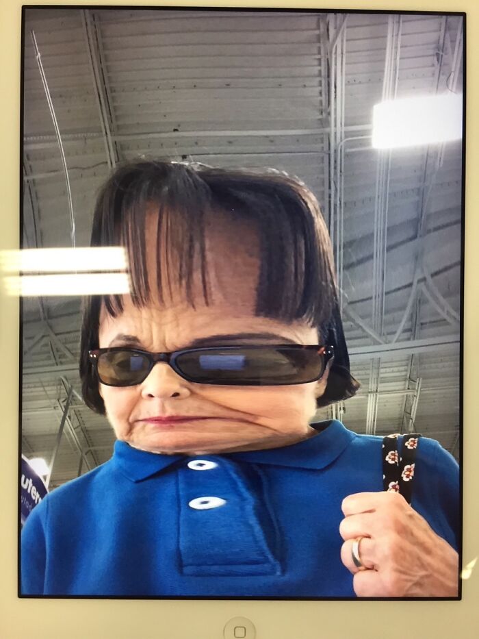 Distorted funny-camera-roll-finds image of a person in sunglasses and a blue shirt, with an exaggerated forehead.