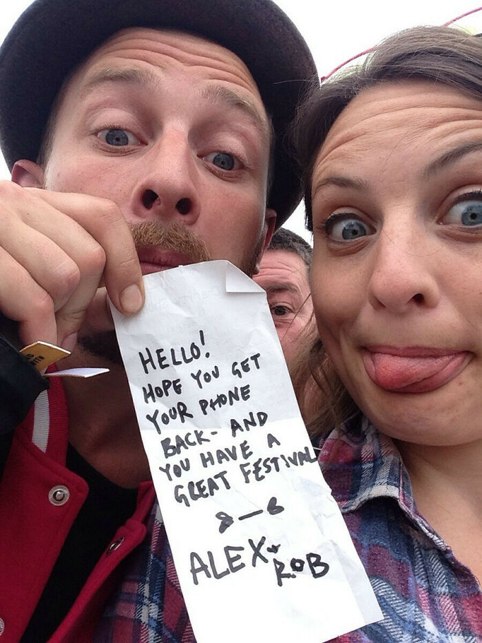 Two people at a festival making funny faces, holding a note with a humorous message.