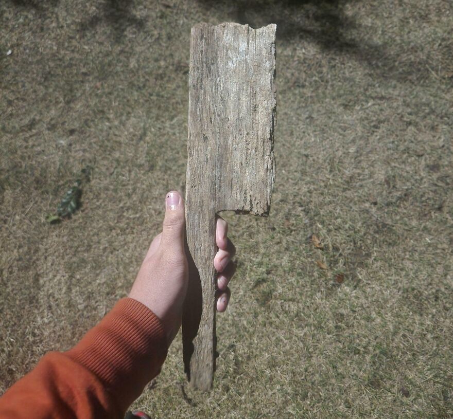 Hand holding a wooden stick resembling an axe on a grass background.