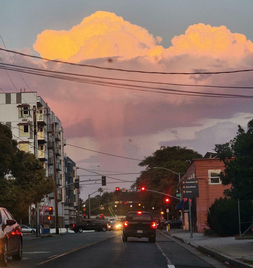 Clouds resembling mountains at sunset over a busy city street with cars and traffic lights.