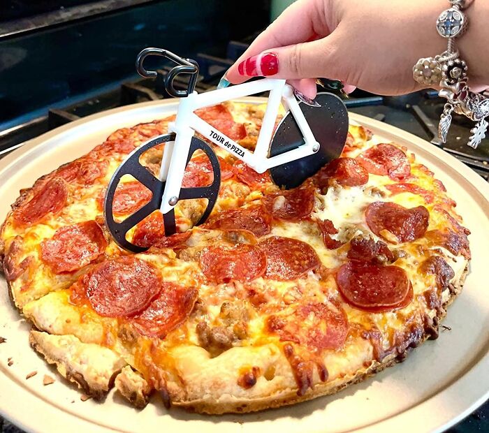 Hand using a bicycle-shaped pizza cutter on a pepperoni pizza, showing a weird kitchen item that works well.