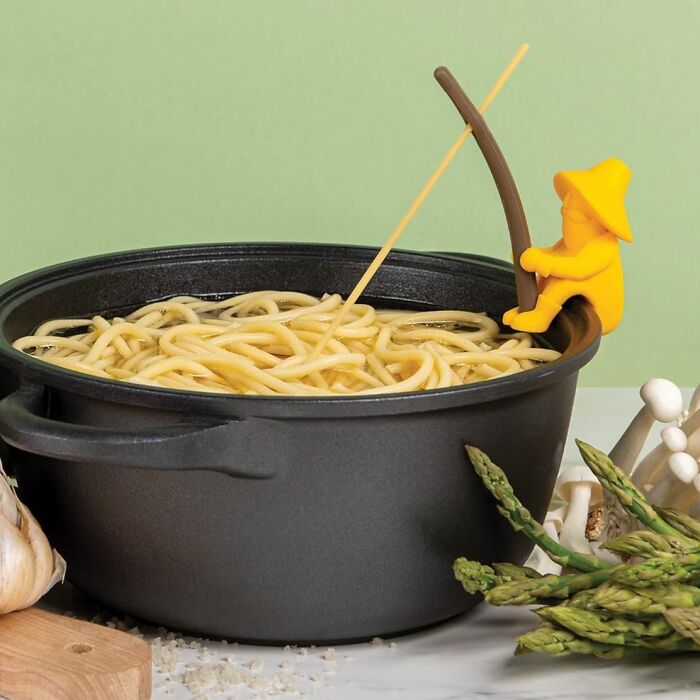 Weird kitchen item: a yellow figure fishing noodle from pot with asparagus and mushrooms.